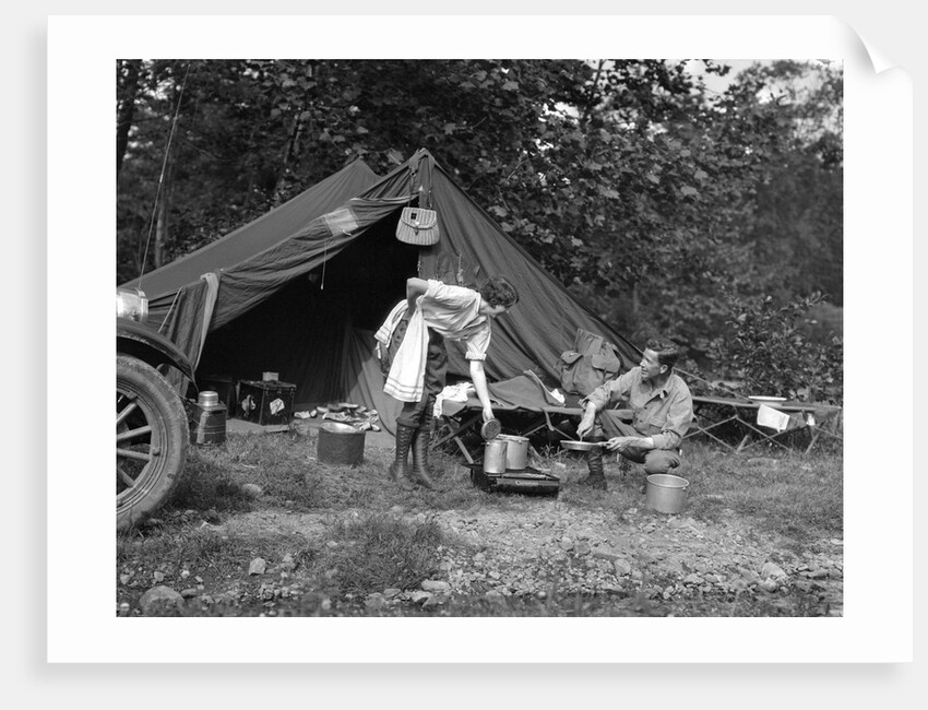 1920s couple man woman on fishing camping trip vacation at campsite man cooking over fire by Anonymous