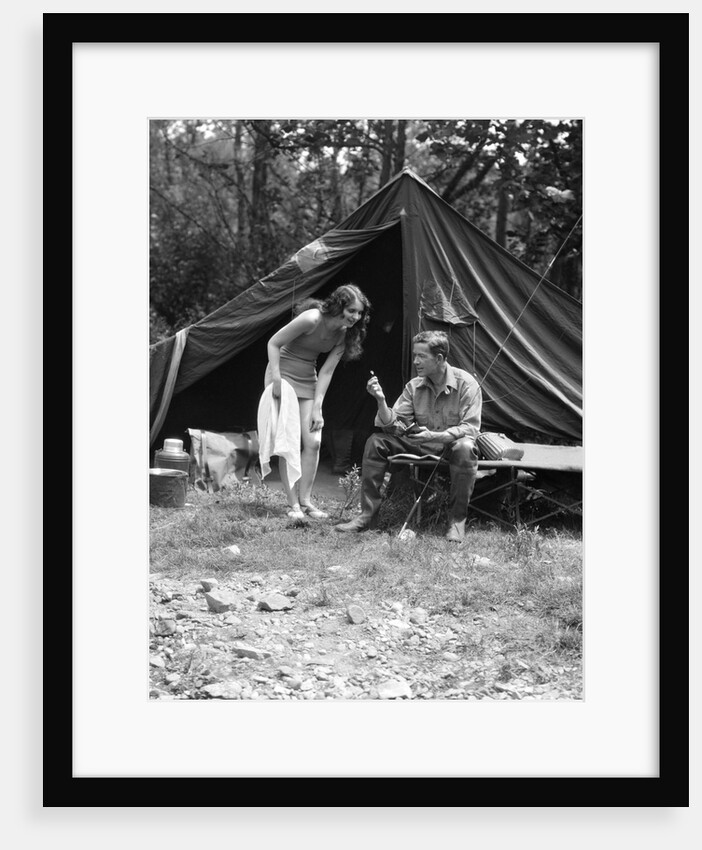 1920s camping couple man sitting by tent with fishing rod woman standing wearing bathing suit by Anonymous