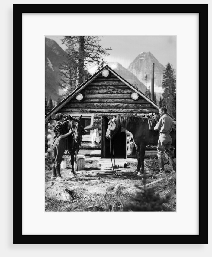 1920s 1930s couple in front of log cabin standing by horses with saddles both wearing jodhpurs assiniboine canada by Anonymous