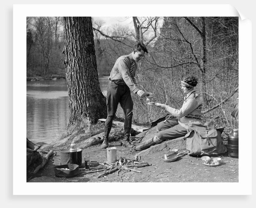 1920s 1930s man & woman camping by lake having picnic woman sitting man standing serving food to woman east creek swamp by Anonymous