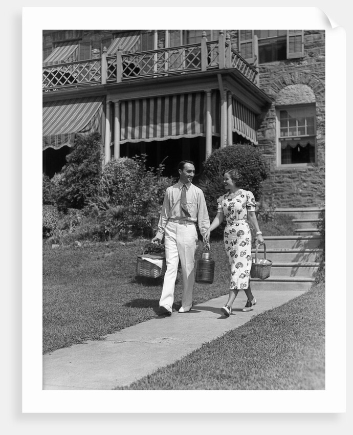 1930s couple walking out of house down sidewalk carrying picnic baskets & thermos jug by Anonymous