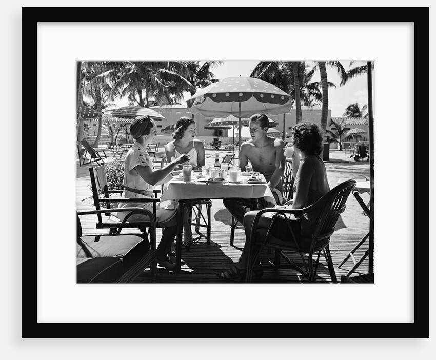 1930s three women and one man sitting at tropical pool side table talking together by Anonymous