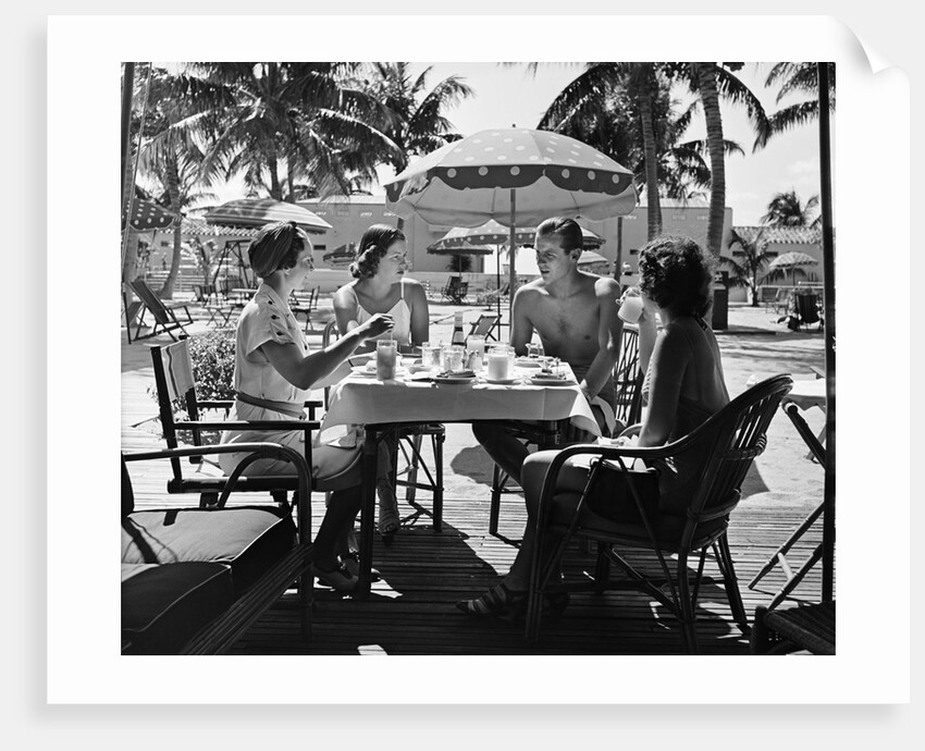 1930s three women and one man sitting at tropical pool side table talking together by Anonymous