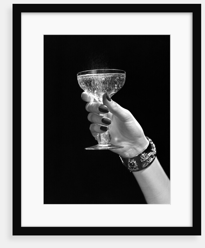 1930s 1940s 1950s woman hand ornate metal bracelet holding up new year toast glass of champagne against black background by Anonymous
