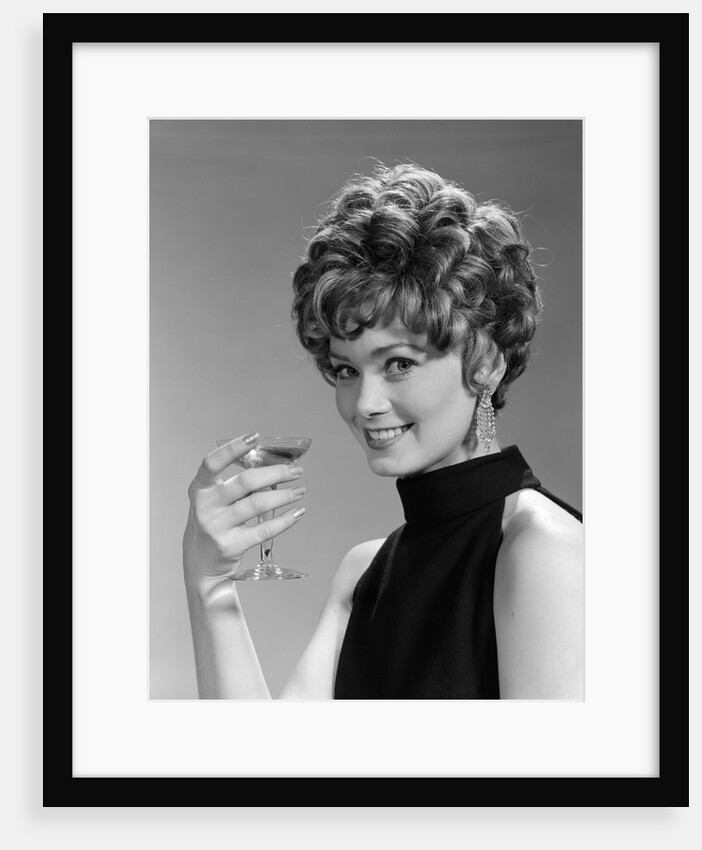 1960s glamorous woman with curly hair and dangling earrings smiling holding a champagne glass looking at camera by Anonymous
