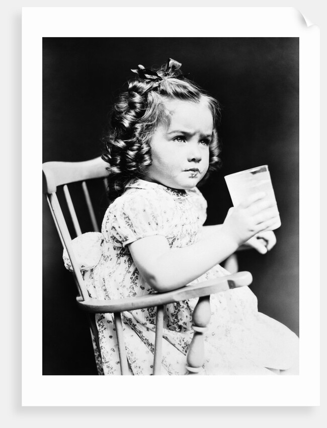 1930s child girl sitting in high chair holding glass of milk serious look bow in hair baloney curls by Anonymous