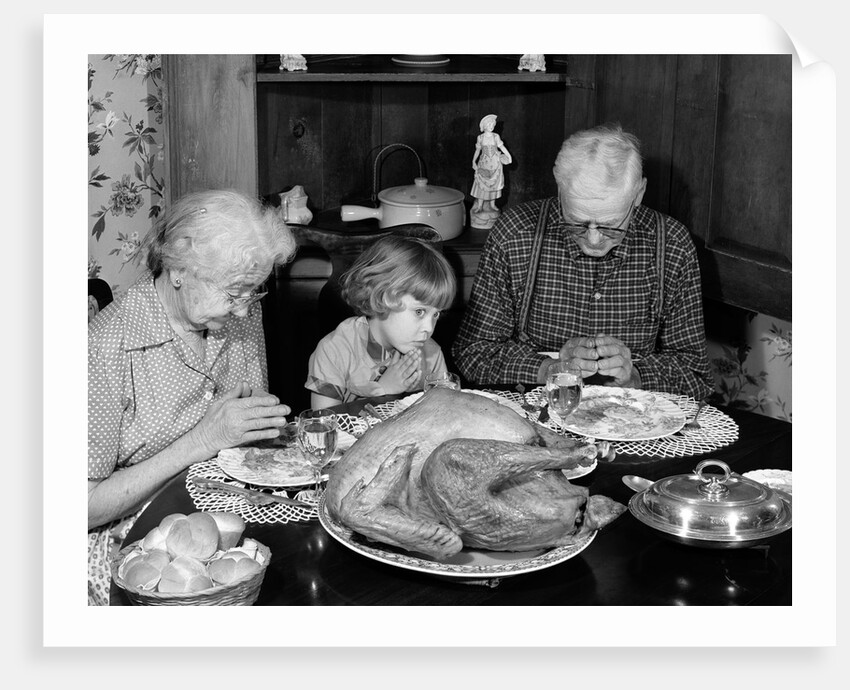 1950s 1960s little girl look at turkey sitting between grandmother grandfather saying grace at table by Anonymous