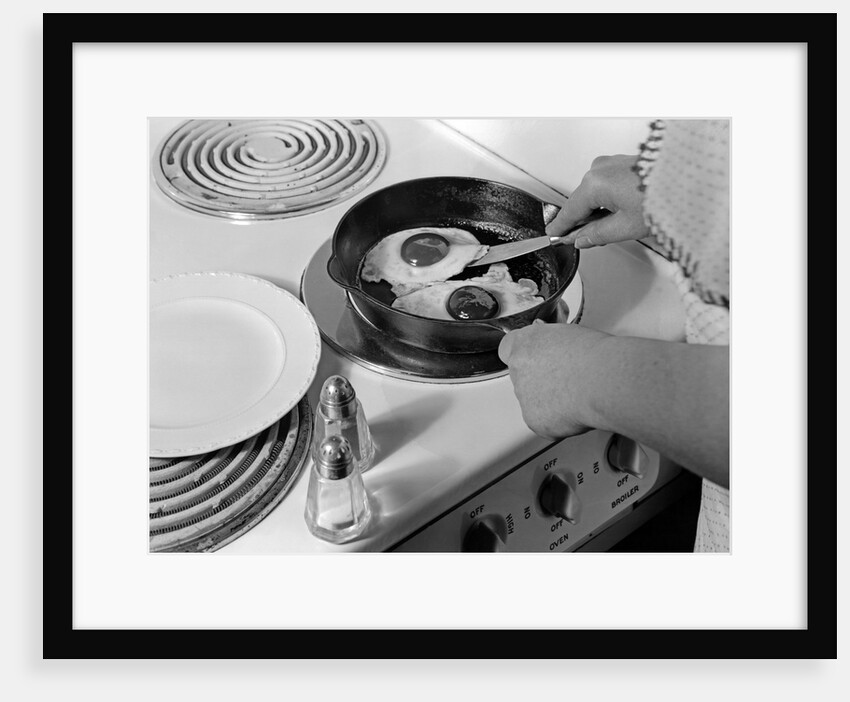 1940s 1950s woman hands frying eggs in iron skillet on electric stove salt and pepper shakers by Anonymous