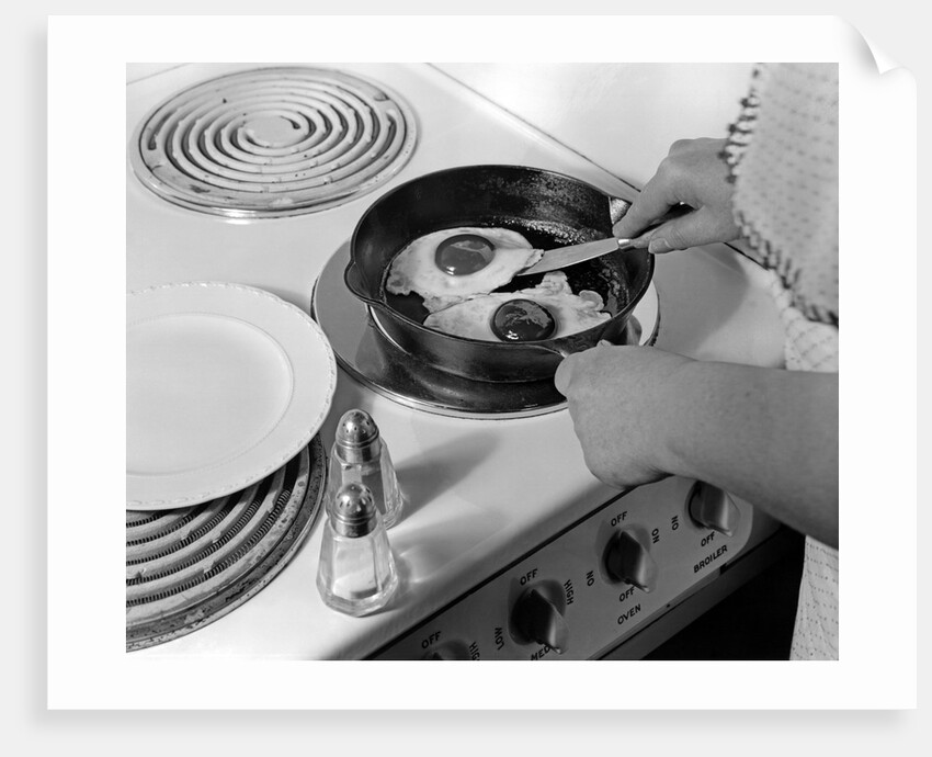 1940s 1950s woman hands frying eggs in iron skillet on electric stove salt and pepper shakers by Anonymous