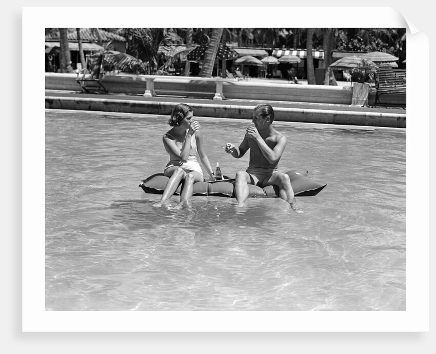 1930s 1940s couple drinking while floating in a pool on a rubber raft at florida resort by Anonymous