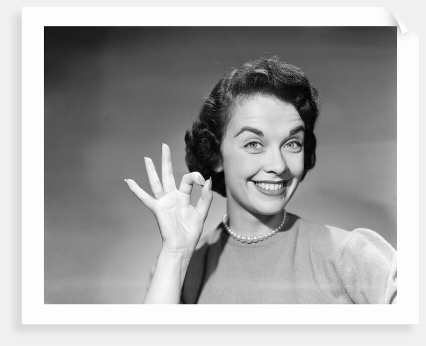1950s woman smiling wearing pearl necklace looking at camera making okay gesture with hand by Anonymous