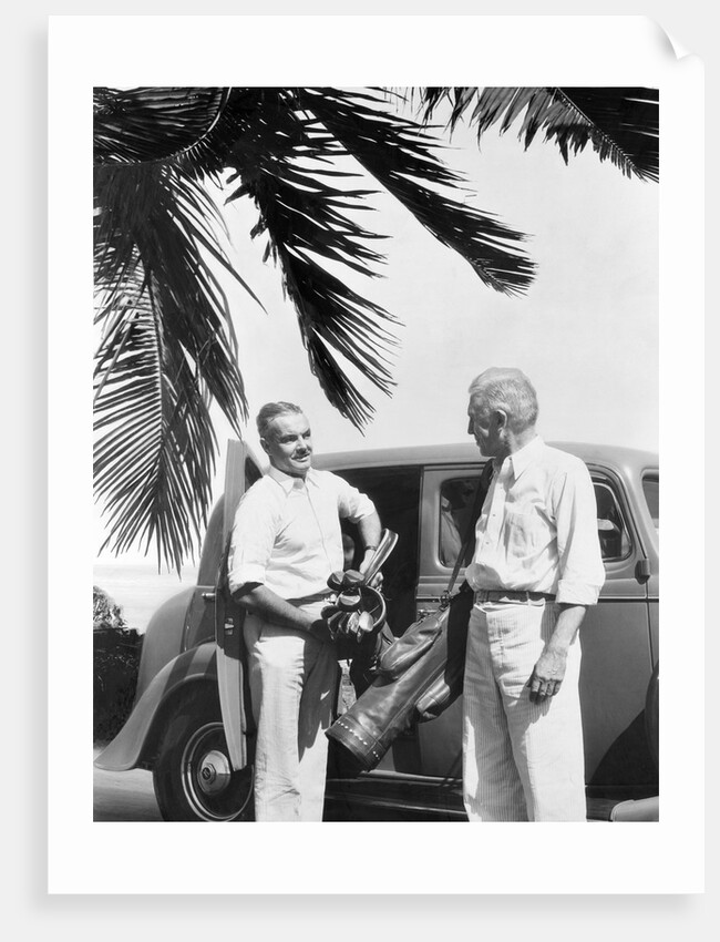 1930s 2 elderly men standing by car carrying golf bag palm tree frond in corner by Anonymous