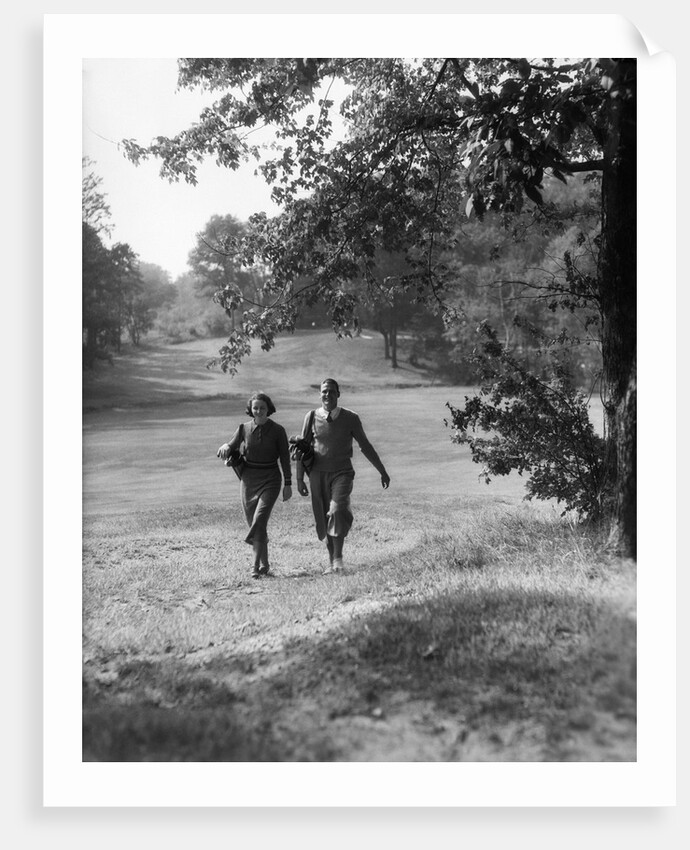 1930s couple man woman each carrying a golf bag walking down the fairway of the golf course by Anonymous