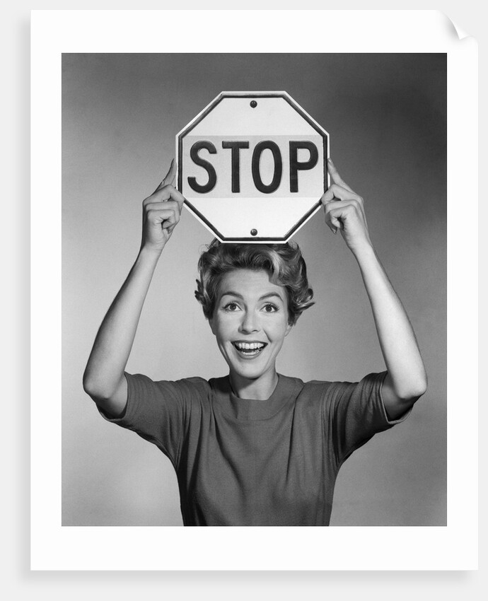 1950s 1960s smiling woman holding stop sign above her head looking at camera by Anonymous