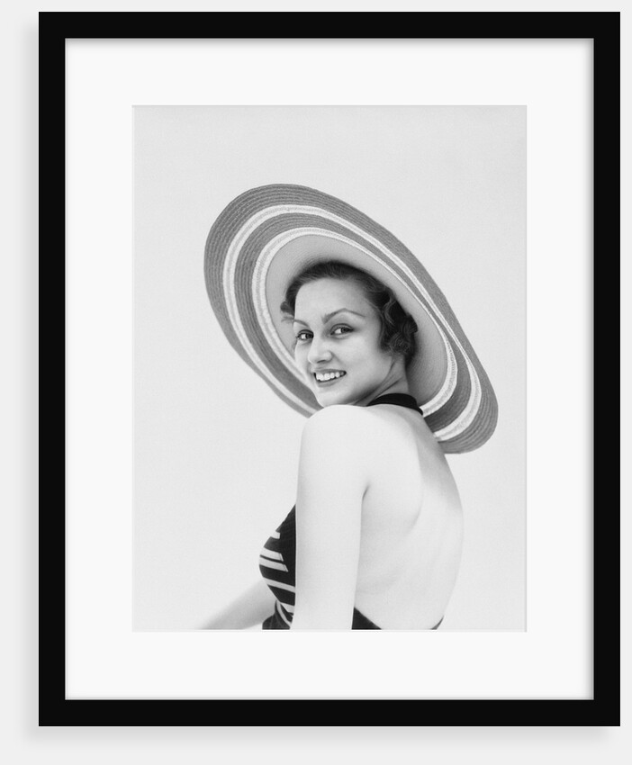 1930s woman wearing striped halter top and very wide brim straw hat looking at camera over shoulder by Anonymous