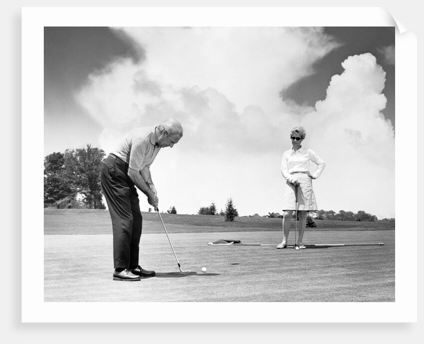 1960s older couple on golfing green man putting by Anonymous