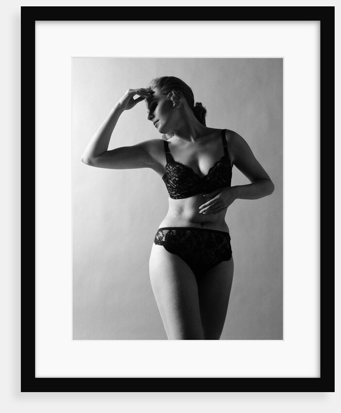1970s woman wearing black lace bra and panties head turned to side hand touching forehead arms in graceful pose indoor by Anonymous