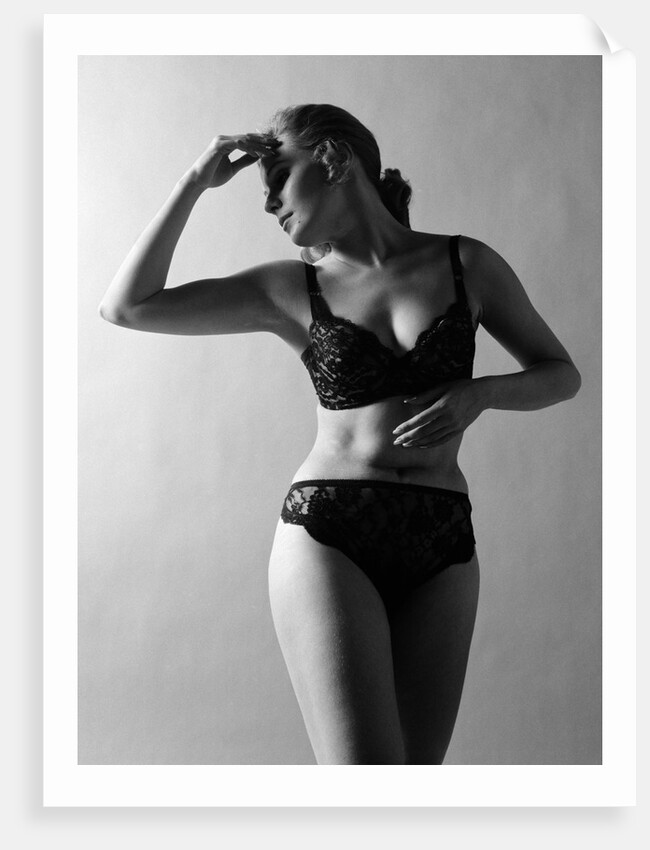 1970s woman wearing black lace bra and panties head turned to side hand touching forehead arms in graceful pose indoor by Anonymous