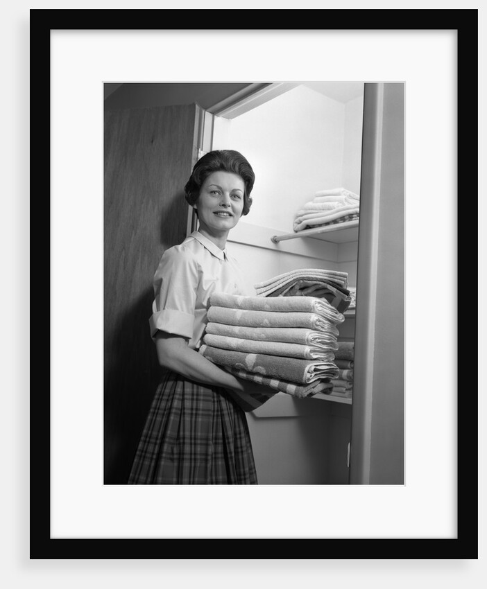 1950s 1960s housewife holding laundry folded towels by linen closet looking at camera by Anonymous