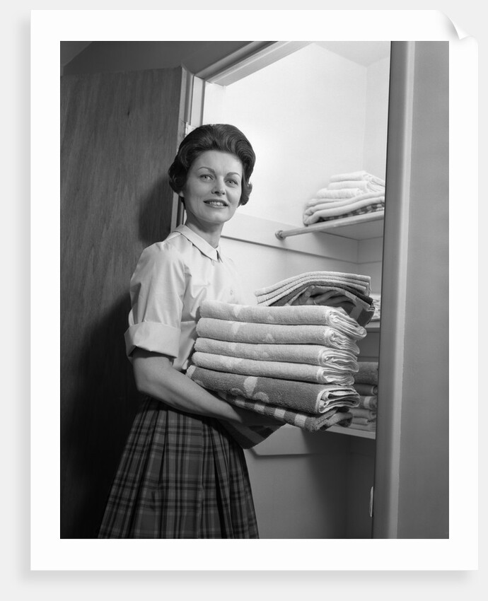 1950s 1960s housewife holding laundry folded towels by linen closet looking at camera by Anonymous