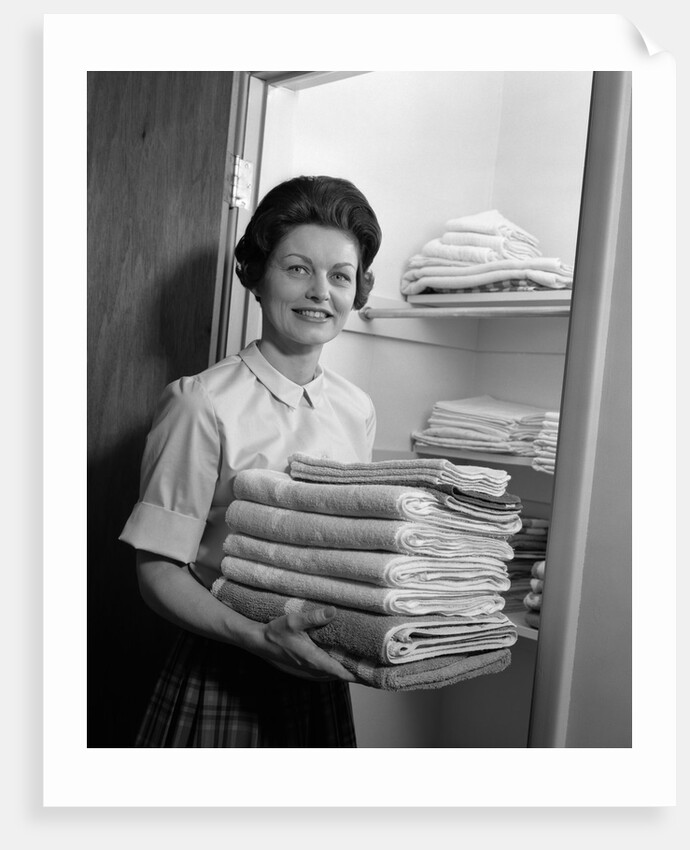 1960s woman holding laundry folded towels by linen closet looking at camera by Anonymous
