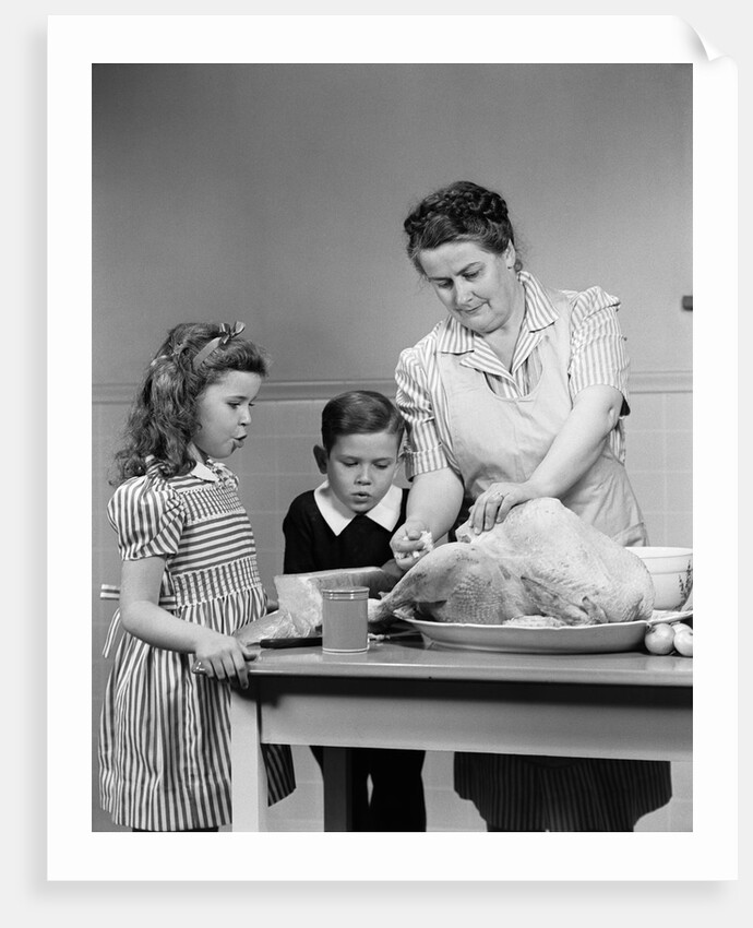 1940s mother son daughter in kitchen stuffing turkey for thanksgiving dinner by Anonymous