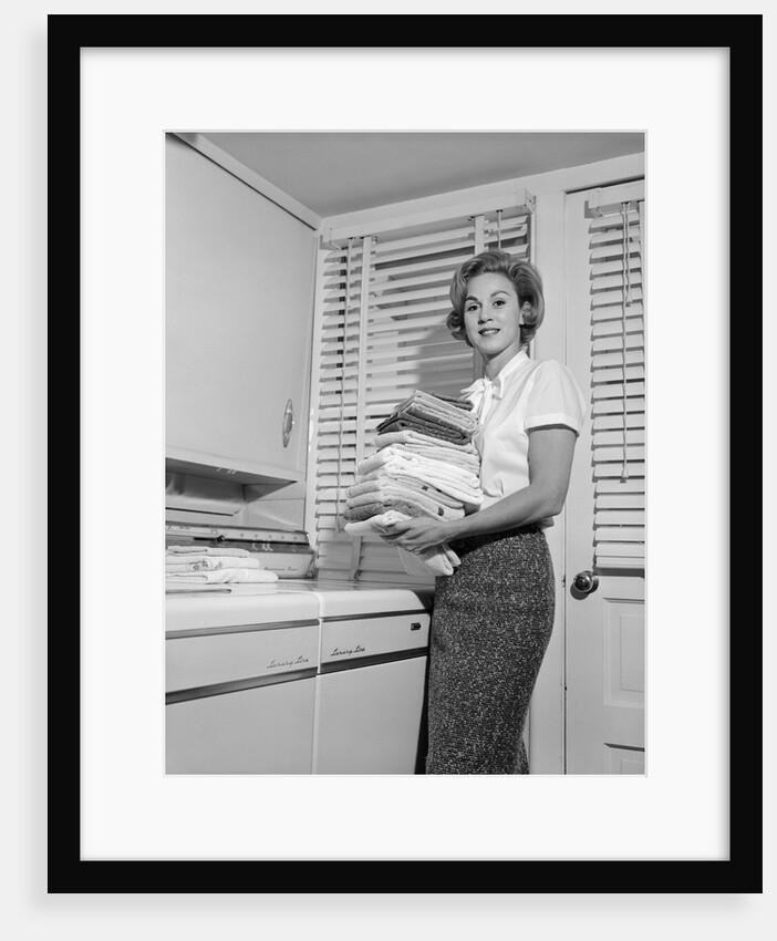 1960s woman holding folded laundry looking at camera by Anonymous