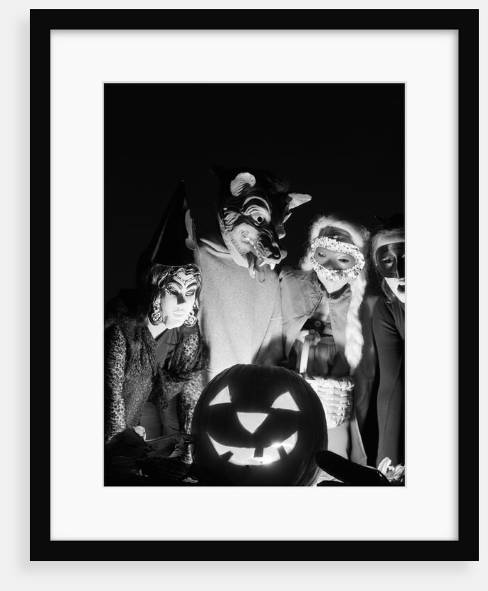 1960s group of four children in halloween costumes gathered around jack-o'-lantern indoor by Anonymous