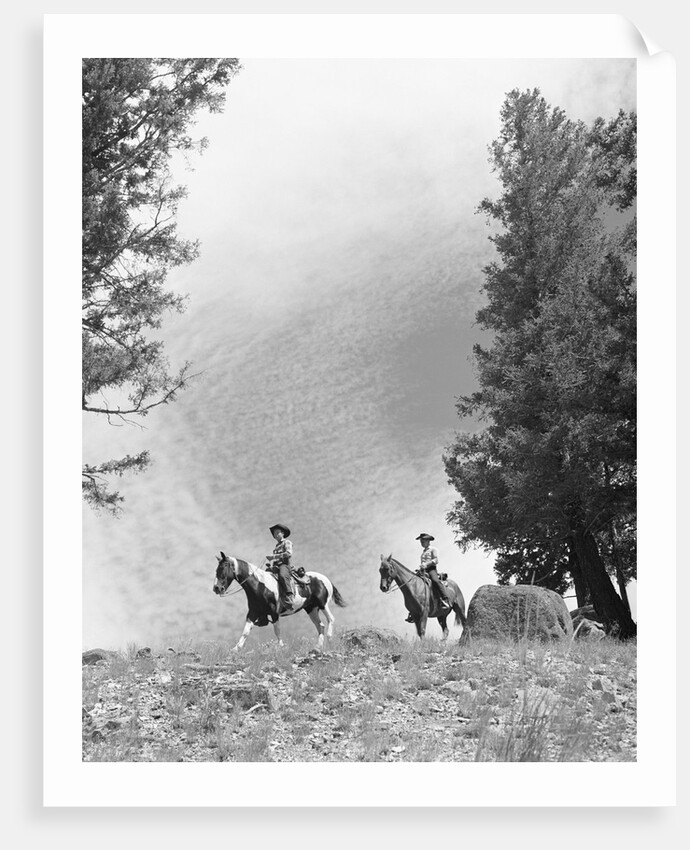 1950s 1960s two men on horseback riding across field wearing cowboy hats by Anonymous