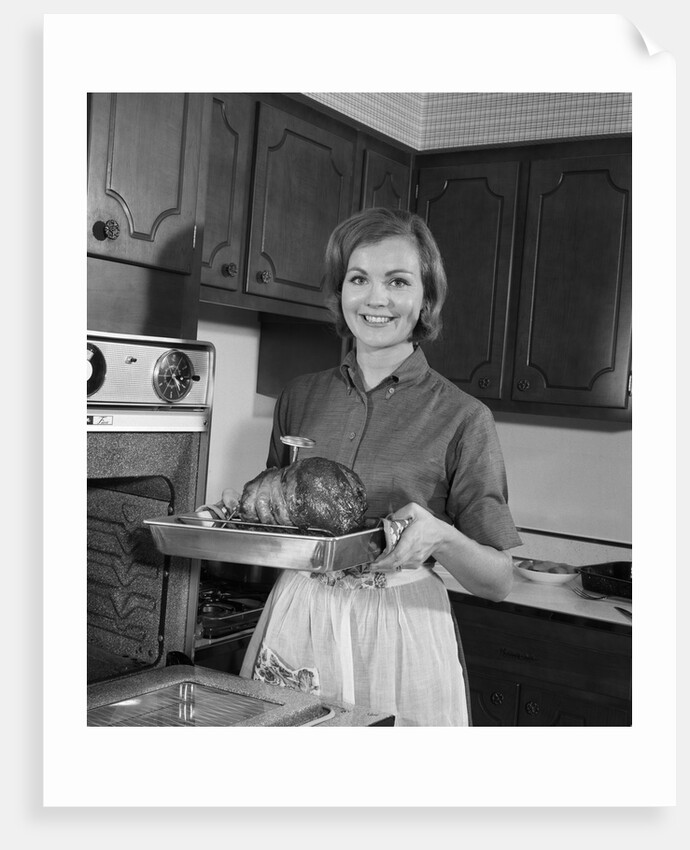 1960s smiling woman in kitchen taking roast out of oven looking at camera by Anonymous