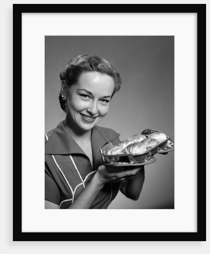 1950s smiling woman holding freshly baked rolls looking at camera by Anonymous