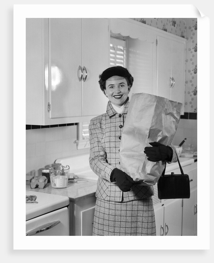 1950s smiling woman in kitchen holding grocery bag handbag wearing hat gloves looking at camera by Anonymous