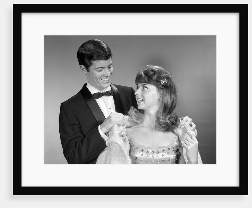 1960s teen couple formally dressed boy helping girl on with coat to go to prom by Anonymous
