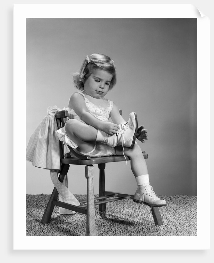 1960s little girl putting on shoes sitting on chair by Anonymous