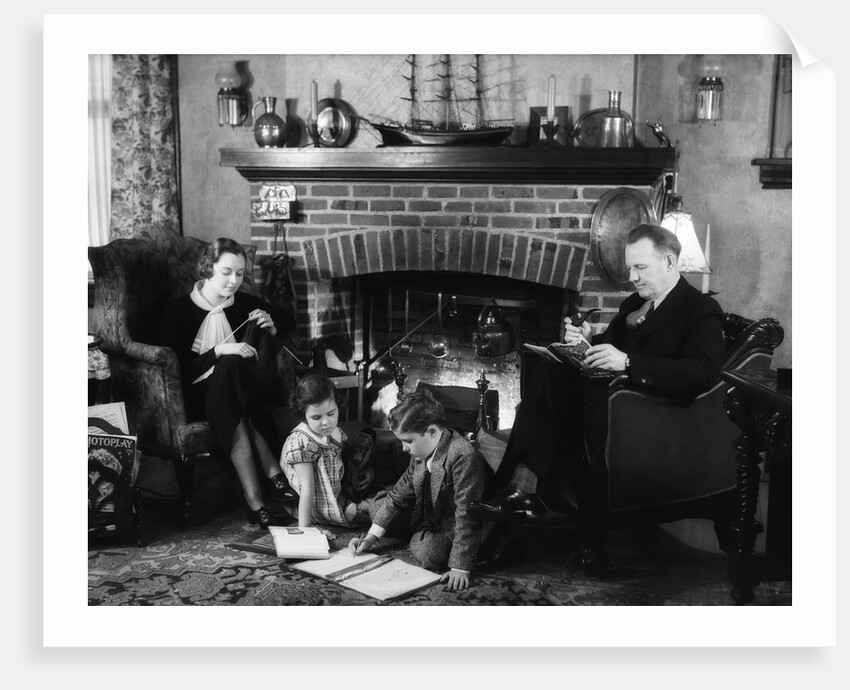 1930s family of four sitting in front fireplace mother knitting father reading smoking pipe kids doing homework by Anonymous