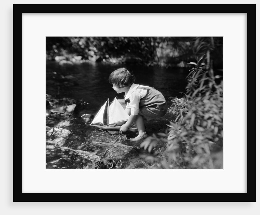 1920s boy putting toy sailboat into stream by Anonymous