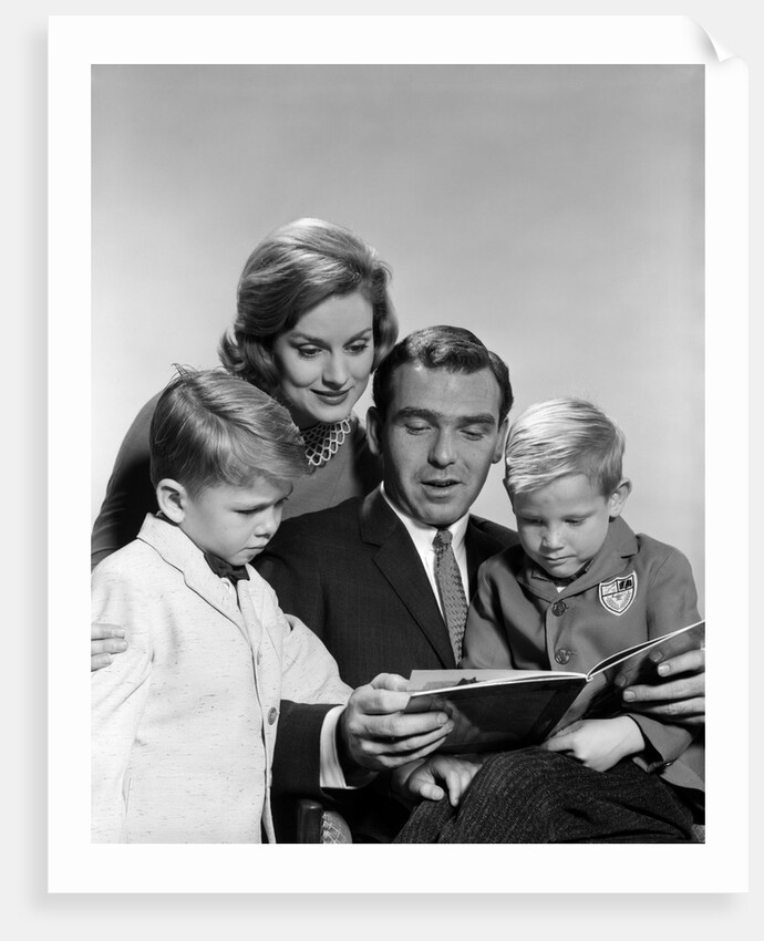 1960s family father mother sons reading book together by Anonymous