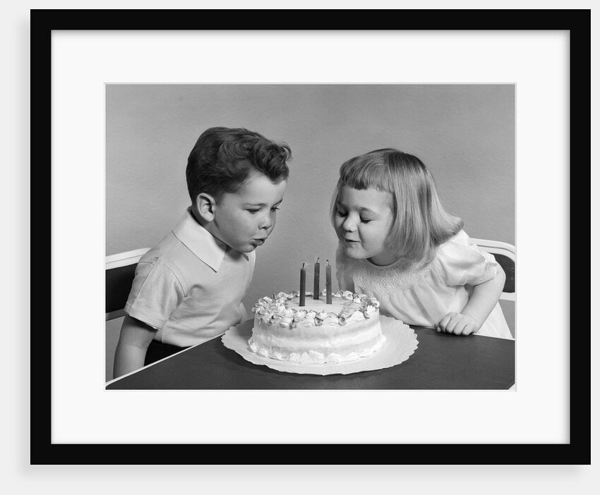 1940s 1950s two children blowing out birthday candles by Anonymous