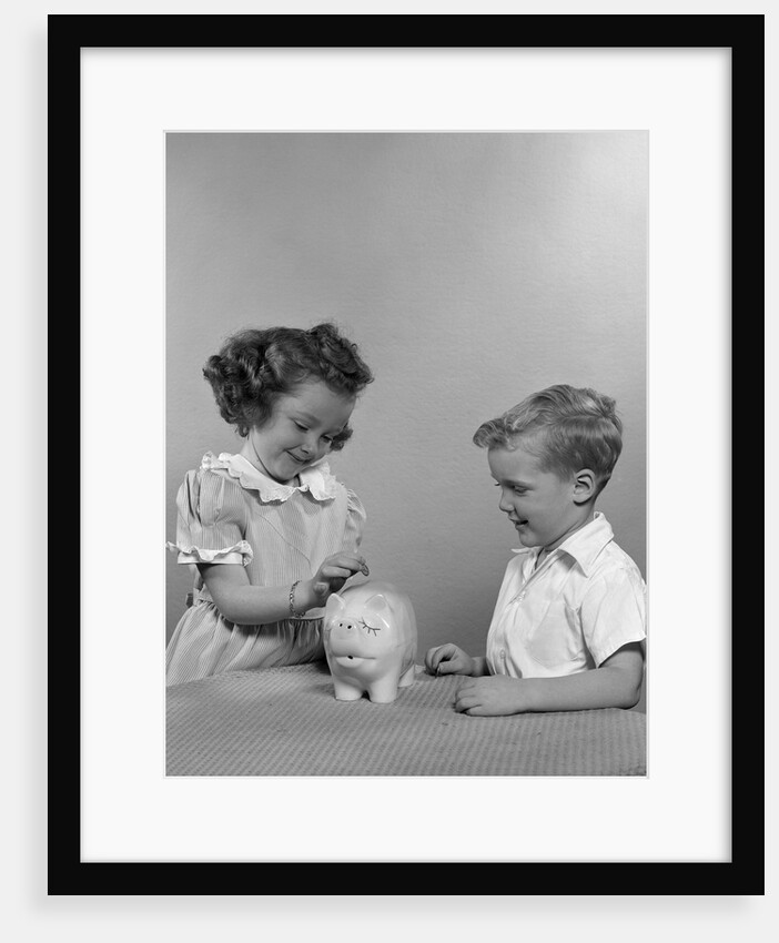 1950s little girl and boy putting coin into piggy bank by Anonymous