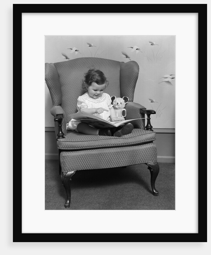 1930s little girl child in large chair with bear reading book by Anonymous