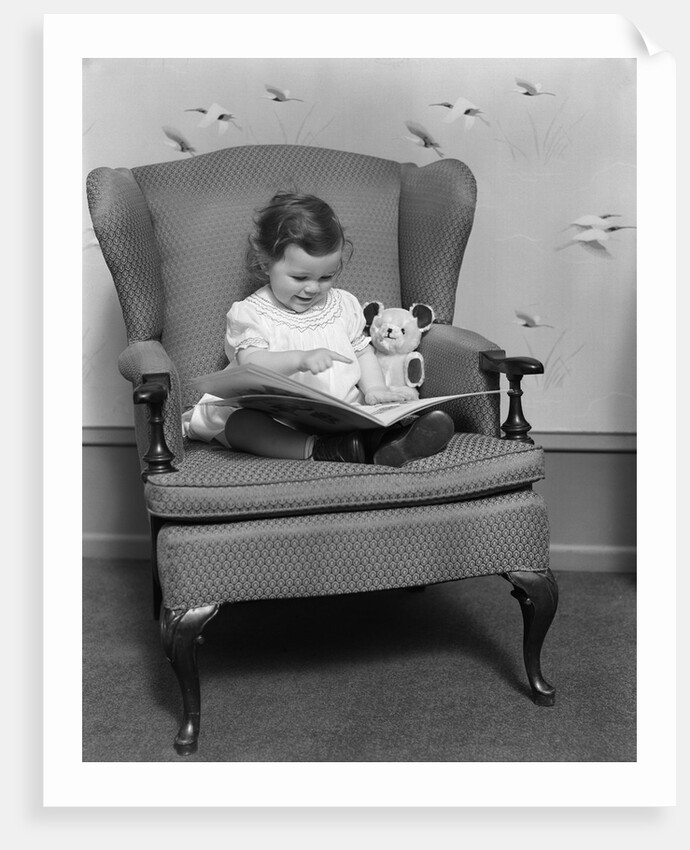1930s little girl child in large chair with bear reading book by Anonymous