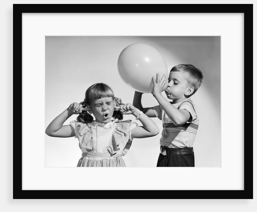 1950s little boy blowing up big balloon little girl with fingers in ears eyes closed by Anonymous