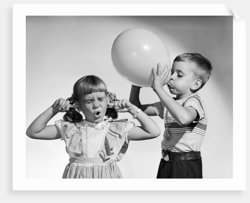 1950s little boy blowing up big balloon little girl with fingers in ears eyes closed by Anonymous