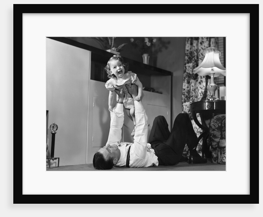 1950s father lying floor holding daughter girl up in the air by Anonymous