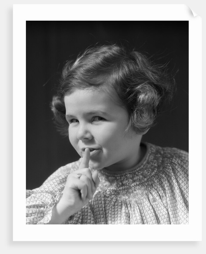 1930s little girl with finger to lips making quiet gesture looking at camera by Anonymous