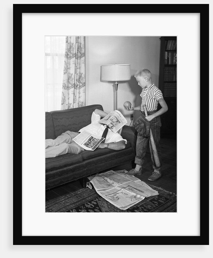 1950s father lying on a sofa with newspaper over his head while son is standing over him with bat ball and baseball glove by Anonymous