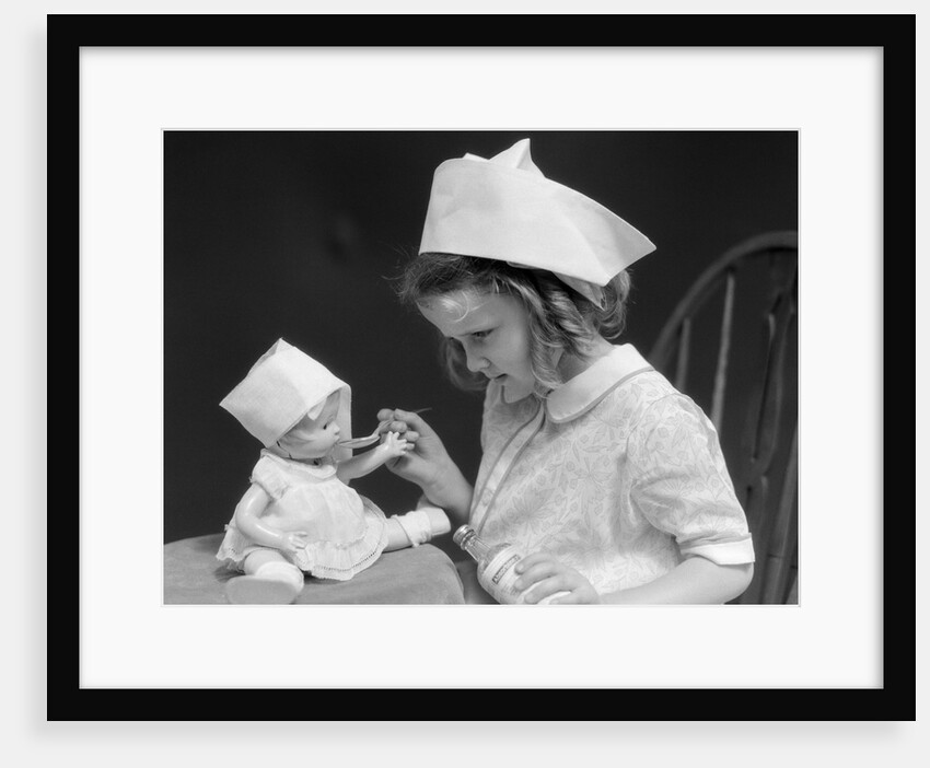 1930s little girl playing nurse with doll spoonful of medicine by Anonymous