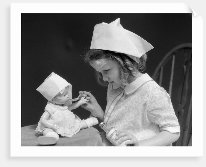 1930s little girl playing nurse with doll spoonful of medicine by Anonymous