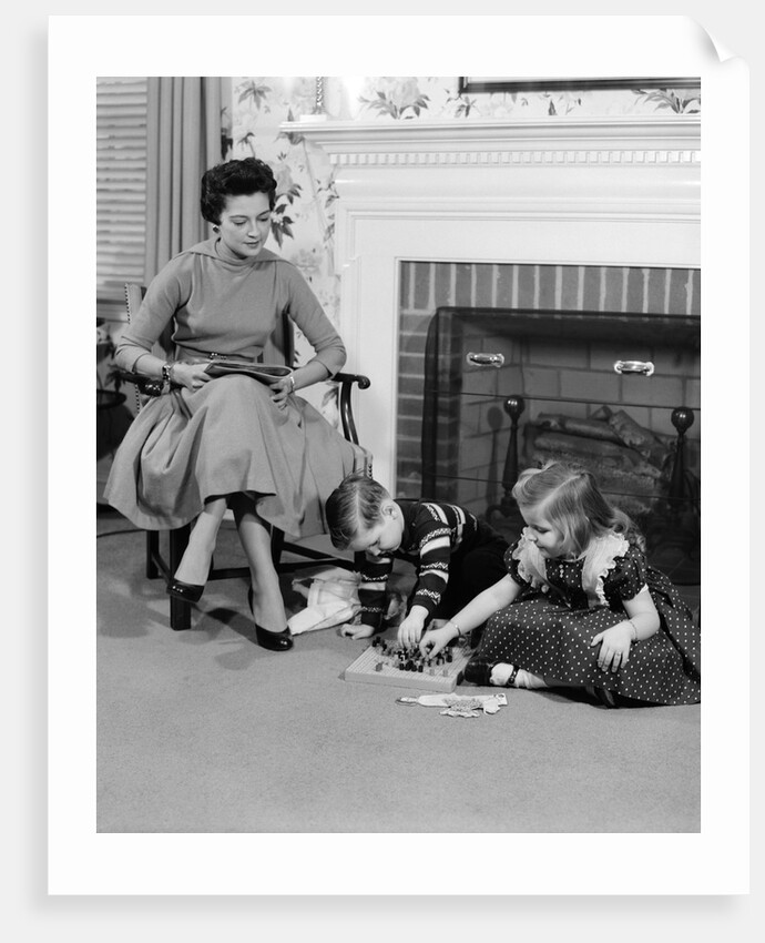 1950s mother watching son daughter playing game in front of fireplace by Anonymous