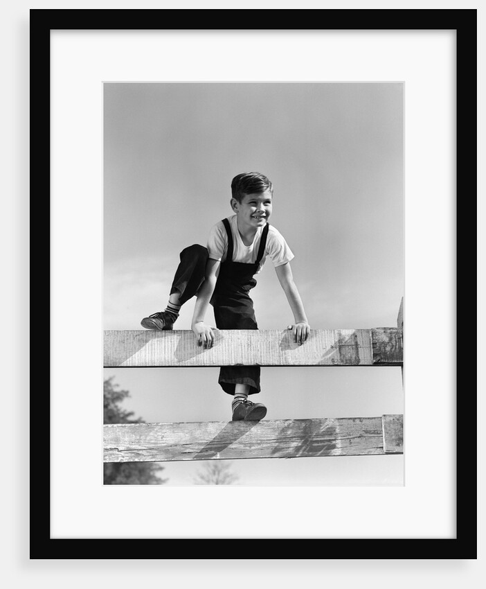 1940s brunette boy wearing overalls climbing over fence by Anonymous